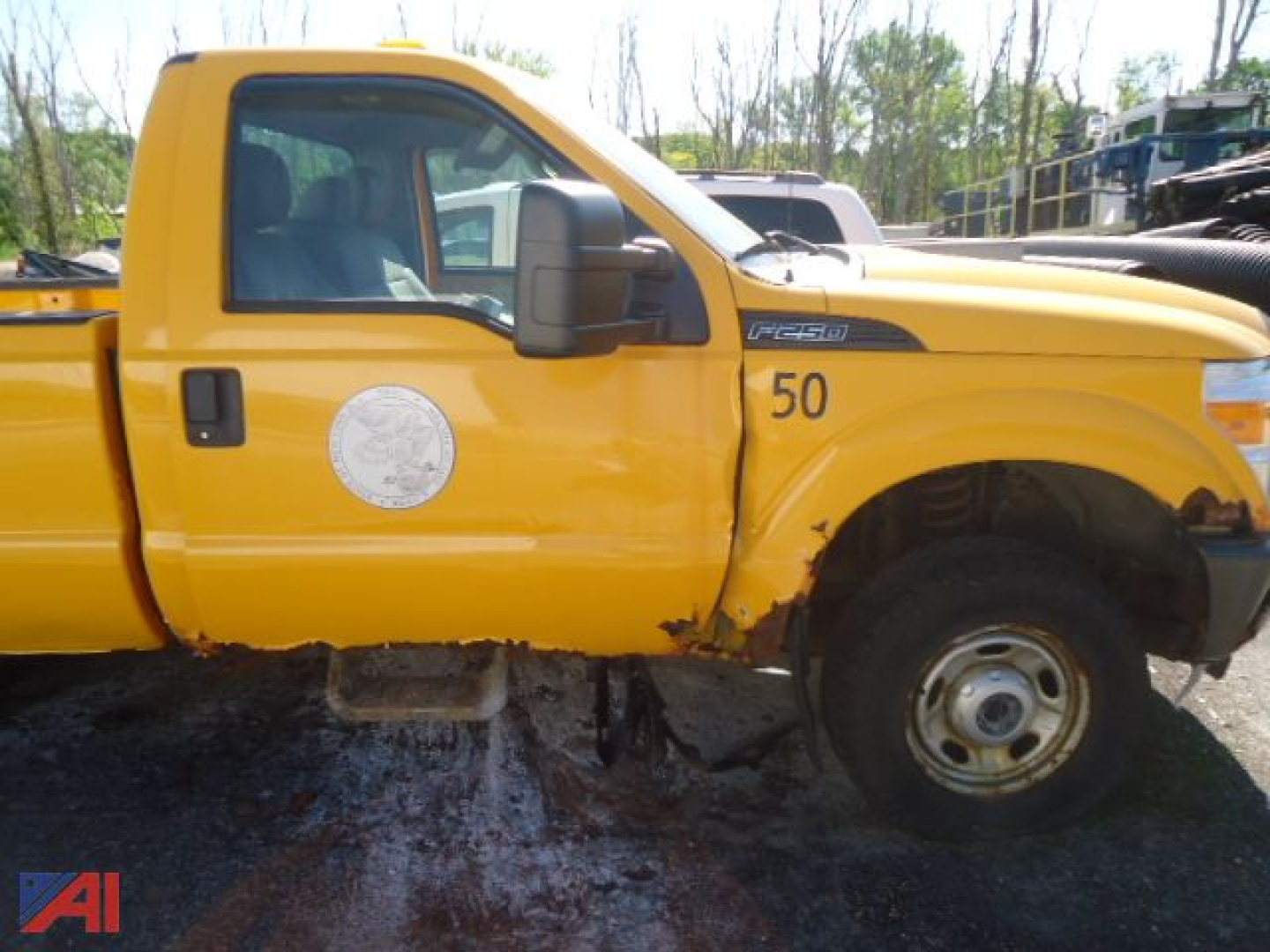 Ford F-250 Super Duty pickup side view showing yellow cab, 50 decal, circular emblems, damaged front fender and wheel well area.