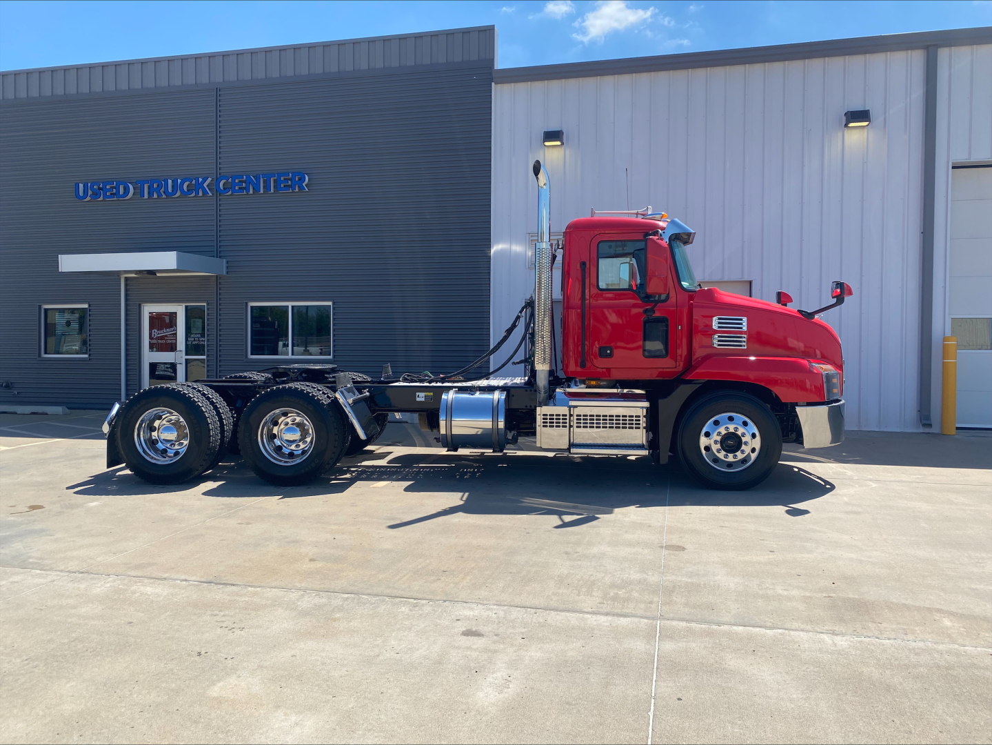 Truck side view of a red 2021 Mack Anthem daycab tractor parked outside a dealership.