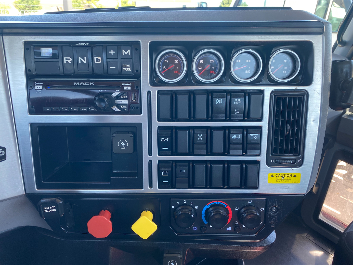 Dashboard view of a 2021 Mack Anthem truck showing instrument gauges, climate controls, radio, and various switches with colored handles.