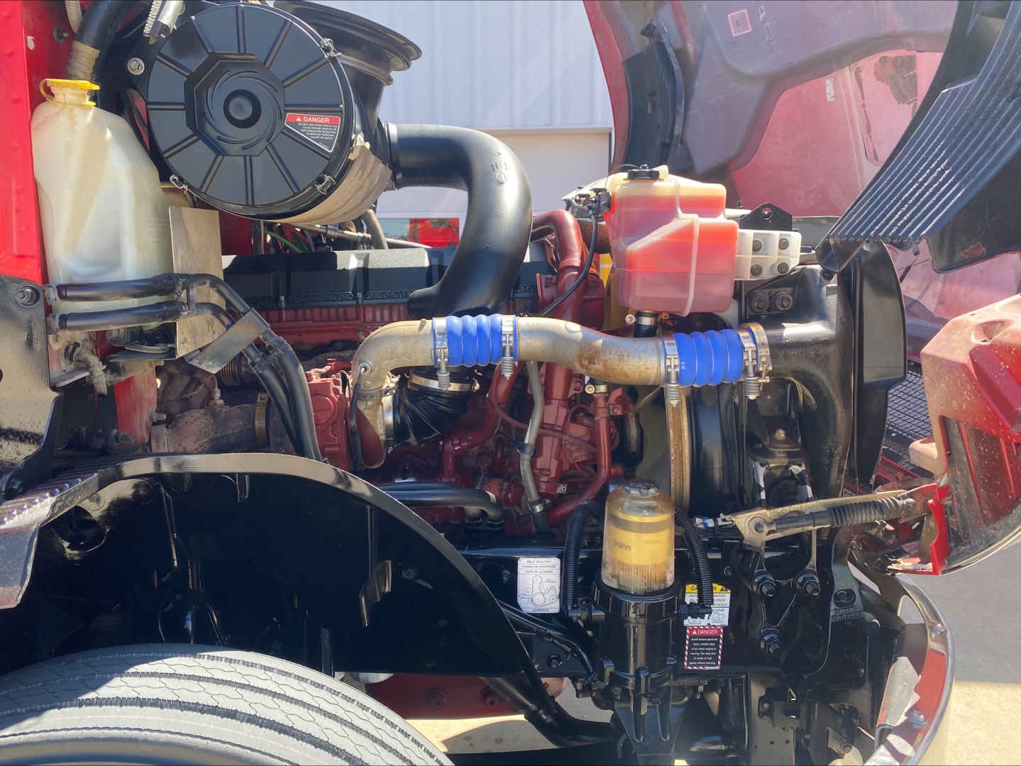 Mack Anthem engine bay showing coolant reservoir, air intake, hoses, and various engine components in a red truck.