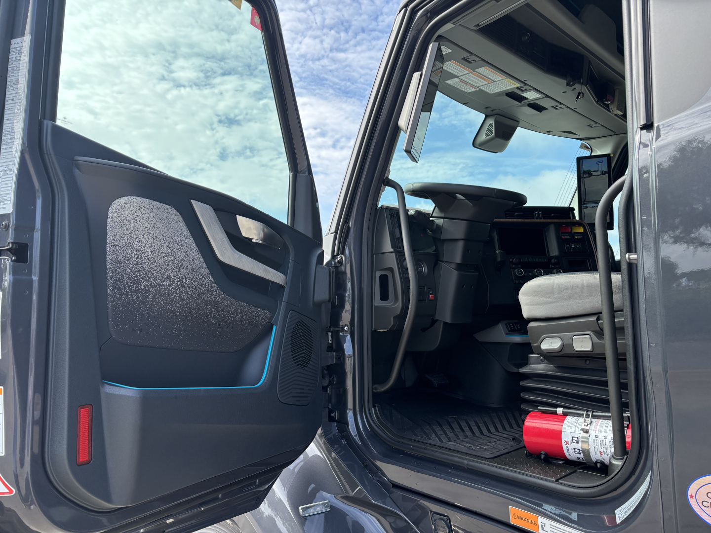 Cab interior of a new Volvo VNL64T860 truck with open door, steering wheel, dashboard, and a fire extinguisher visible.