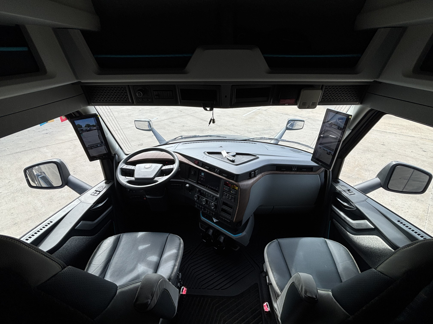 Volvo VNL64T860 truck cabin interior, front dashboard with two screens, steering wheel, driver's seat and passenger seat visible.