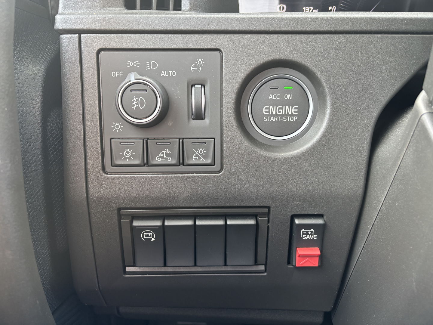 Volvo dashboard area showing headlight switch, engine start-stop button, and a row of additional control buttons.