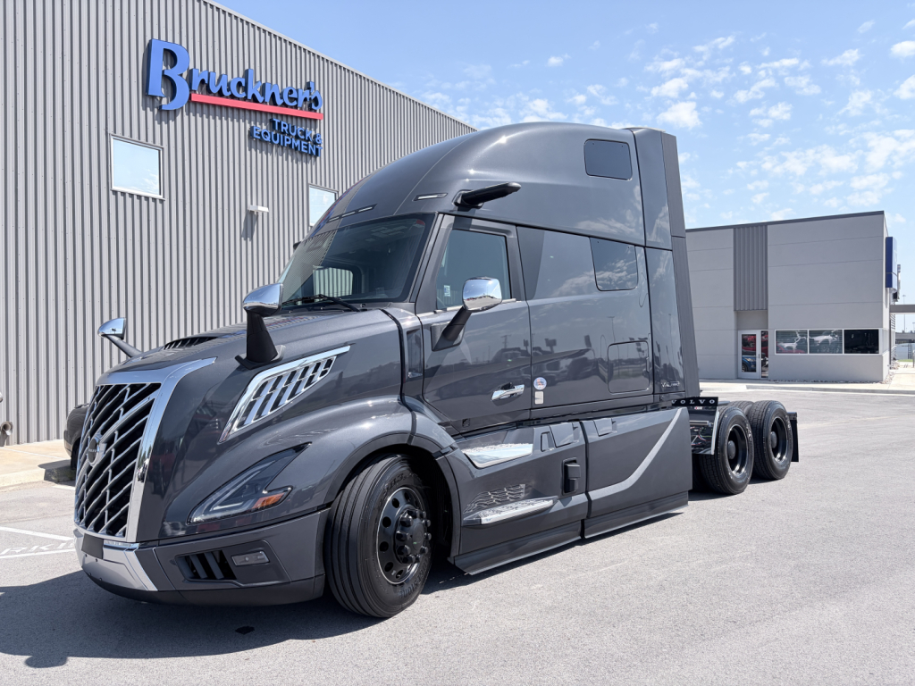 2027 Volvo VNL64T860 truck in front of dealership showing cab with high sleeper and stacked exhausts, external mirrors, and front grille.