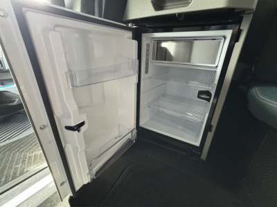 Volvo VNL64T860 new truck interior showing open under-cab refrigerator/freezer and empty small freezer with shelves.