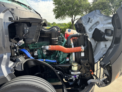 Volvo VNL64T860 engine bay view with orange air intake hose, green engine block, and various hoses and components visible.