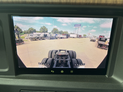Rear cab view of a Volvo VNL truck chassis in a lot, with a drive axle and fifth wheel visible; building and other trucks in background.