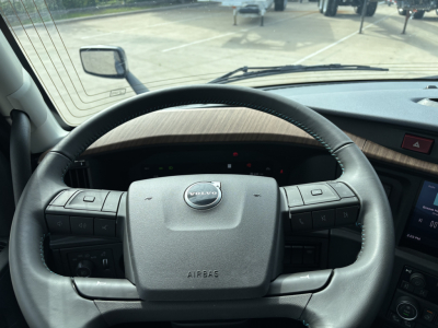 Volvo truck interior steering wheel and dashboard view showing Volvo logo on airbag cover, windshield, and driver-side controls.