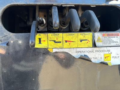 Trailer jack/lever panel showing IN, LOWER, LOWER, RETRACT levers with yellow labels and warning sticker; hydraulic tail control area on a Trail-Eze 40-ton trailer.
