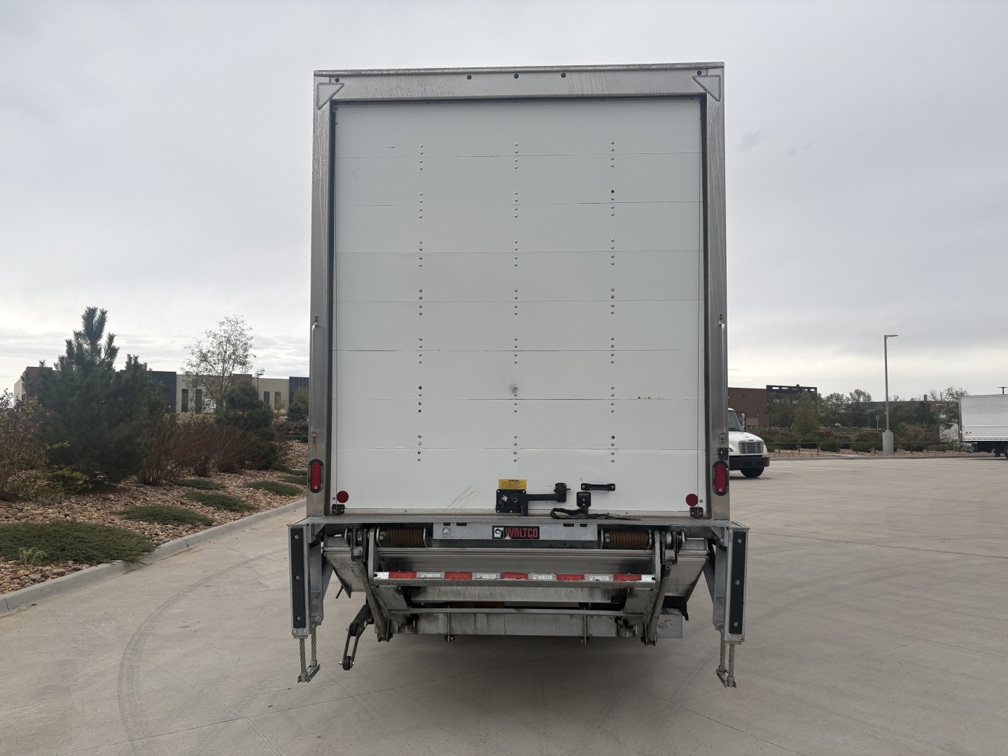 Kenworth T270 box truck rear view showing liftgate and tail/marker lights. Visible text on the rear includes a red/white warning label and mechanical hardware.