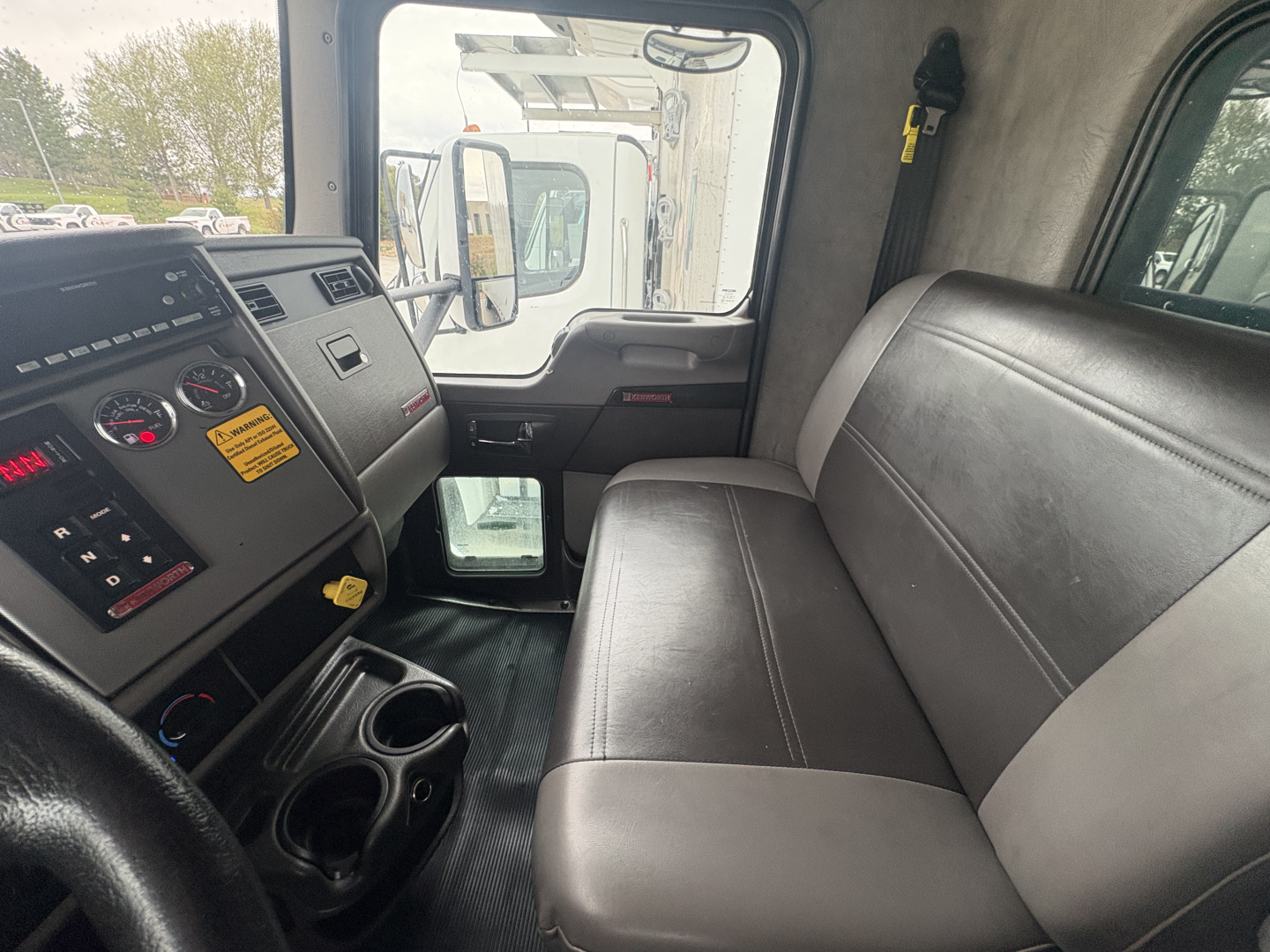 Truck cabin interior showing driver's seat and passenger bench with dashboard controls and cup holders.