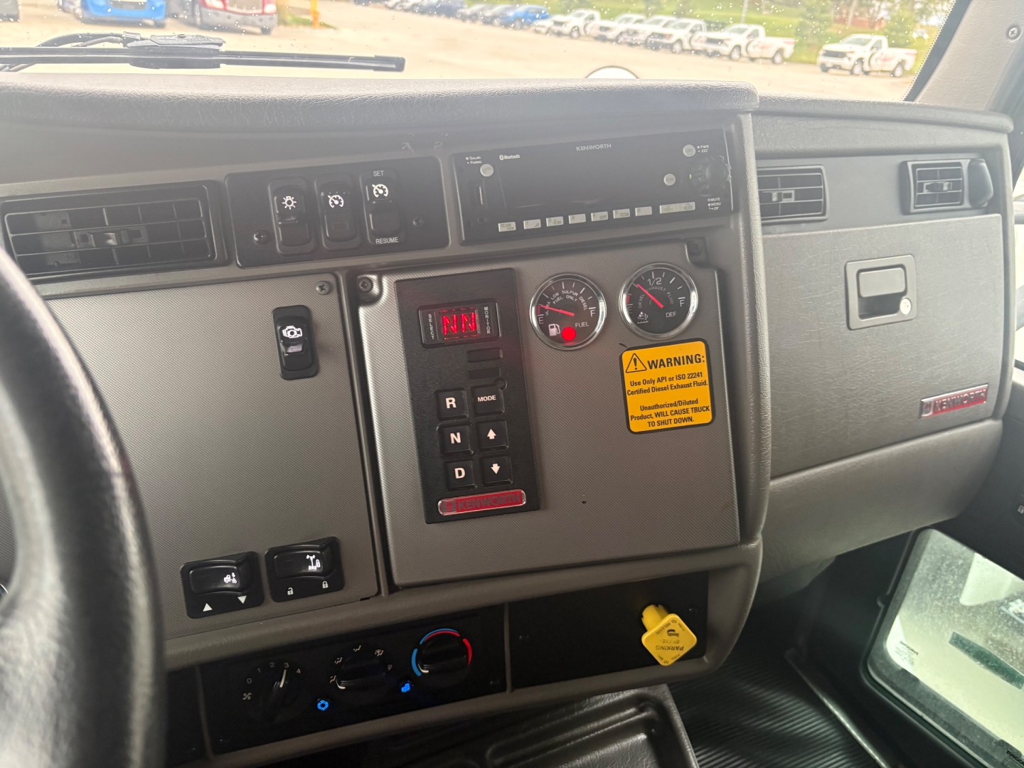 Kenworth T270 cab interior dashboard showing gear shifter panel, warning sticker, gauges, and control knobs.