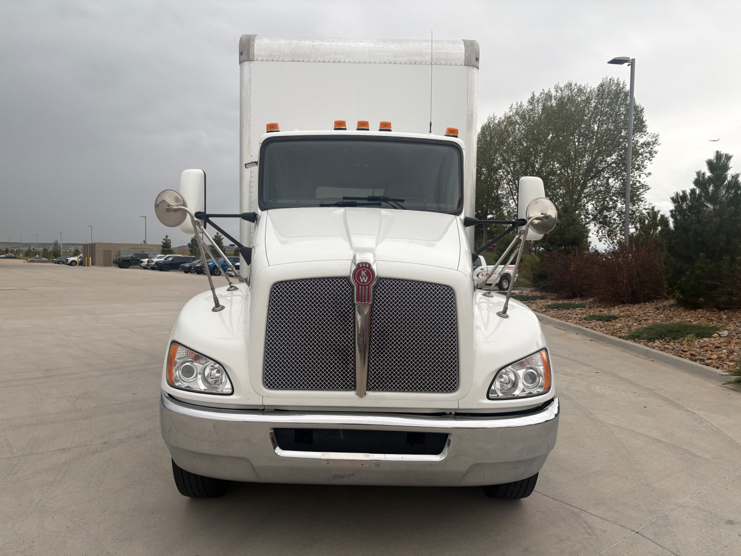 Kenworth T270 front view showing large chrome grille, hood, and dual round mirrors. Vehicle sits on concrete, daytime, white cab with grille emblem visible.