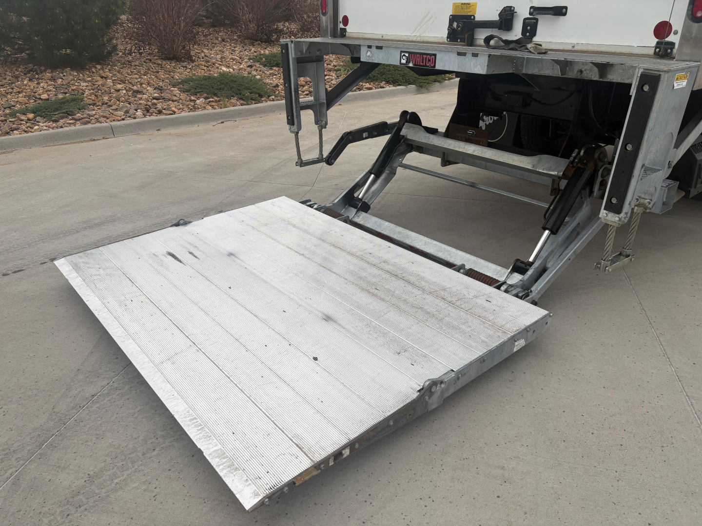 Truck rear with aluminum liftgate extended from box truck showing platform and hydraulic arms