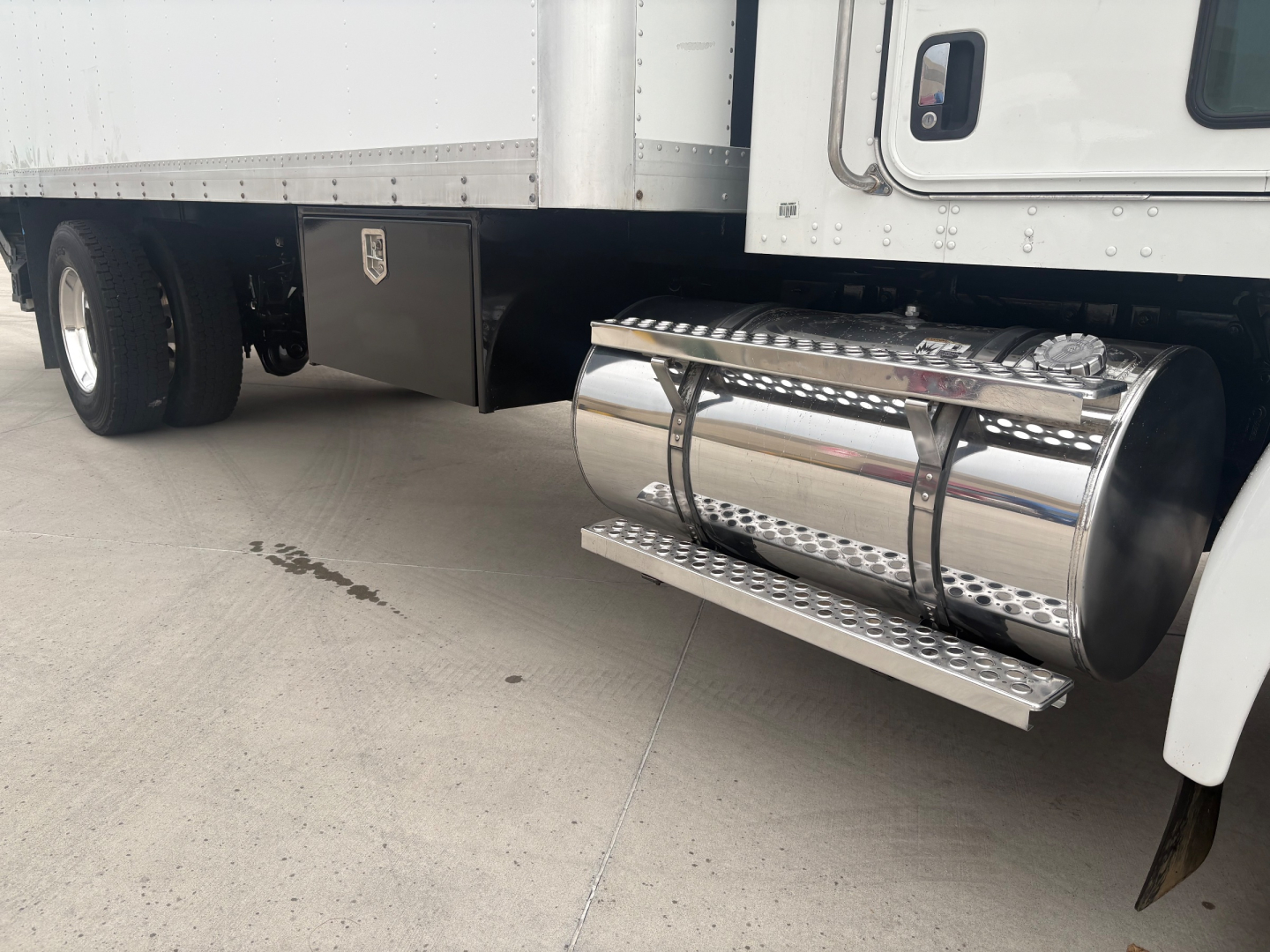 Truck side view showing polished cylindrical fuel tank under the driver side with chrome steps and wheel in background.