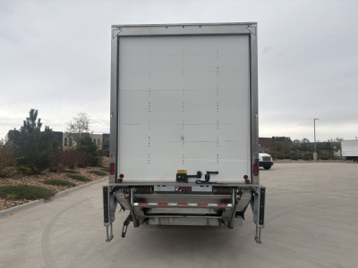 Kenworth T270 box truck rear view showing liftgate and tail/marker lights. Visible text on the rear includes a red/white warning label and mechanical hardware.