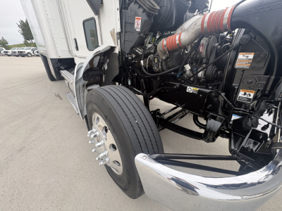 Kenworth T270 front-left wheel and chassis showing front bumper, engine bay, and vertical exhaust pipe in a box truck. Visible components include large front tire, wheel hub, chrome bumper, framed cab step, and hydraulic lines.
