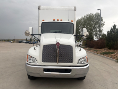 Kenworth T270 front view showing large chrome grille, hood, and dual round mirrors. Vehicle sits on concrete, daytime, white cab with grille emblem visible.