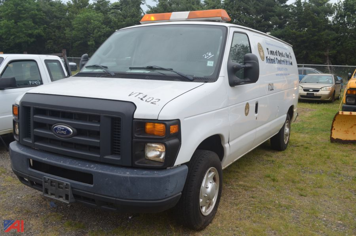 Ford E-Series Econoline cargo van, 2011 model, white, light bar on roof, front grille with Ford emblem, text on side door, parked in lot.