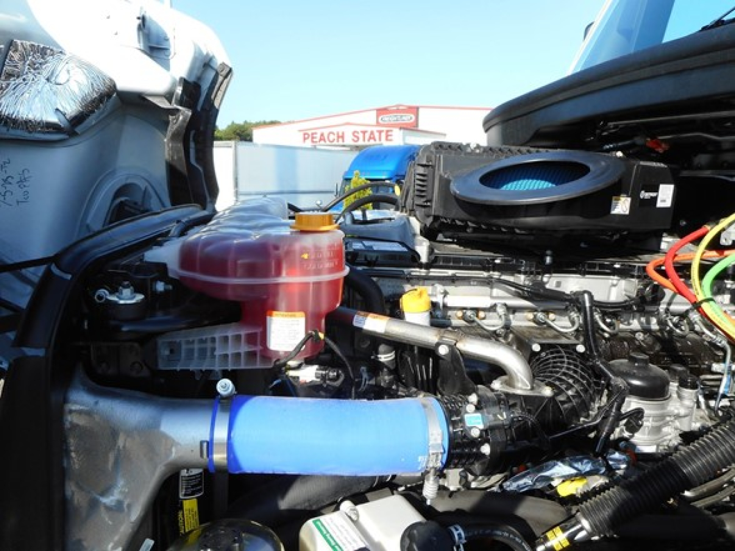 Freightliner Cascadia engine bay showing coolant reservoir, blue hose, and various engine components under open hood.