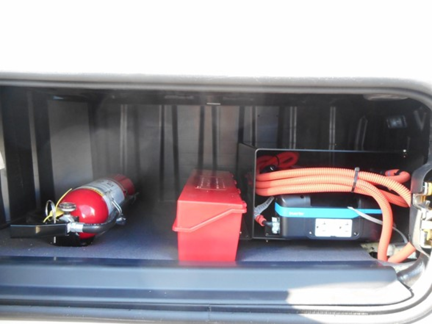 Freightliner Cascadia 126 engine bay area showing battery, orange cables, red battery box, and a red fire extinguisher canister.
