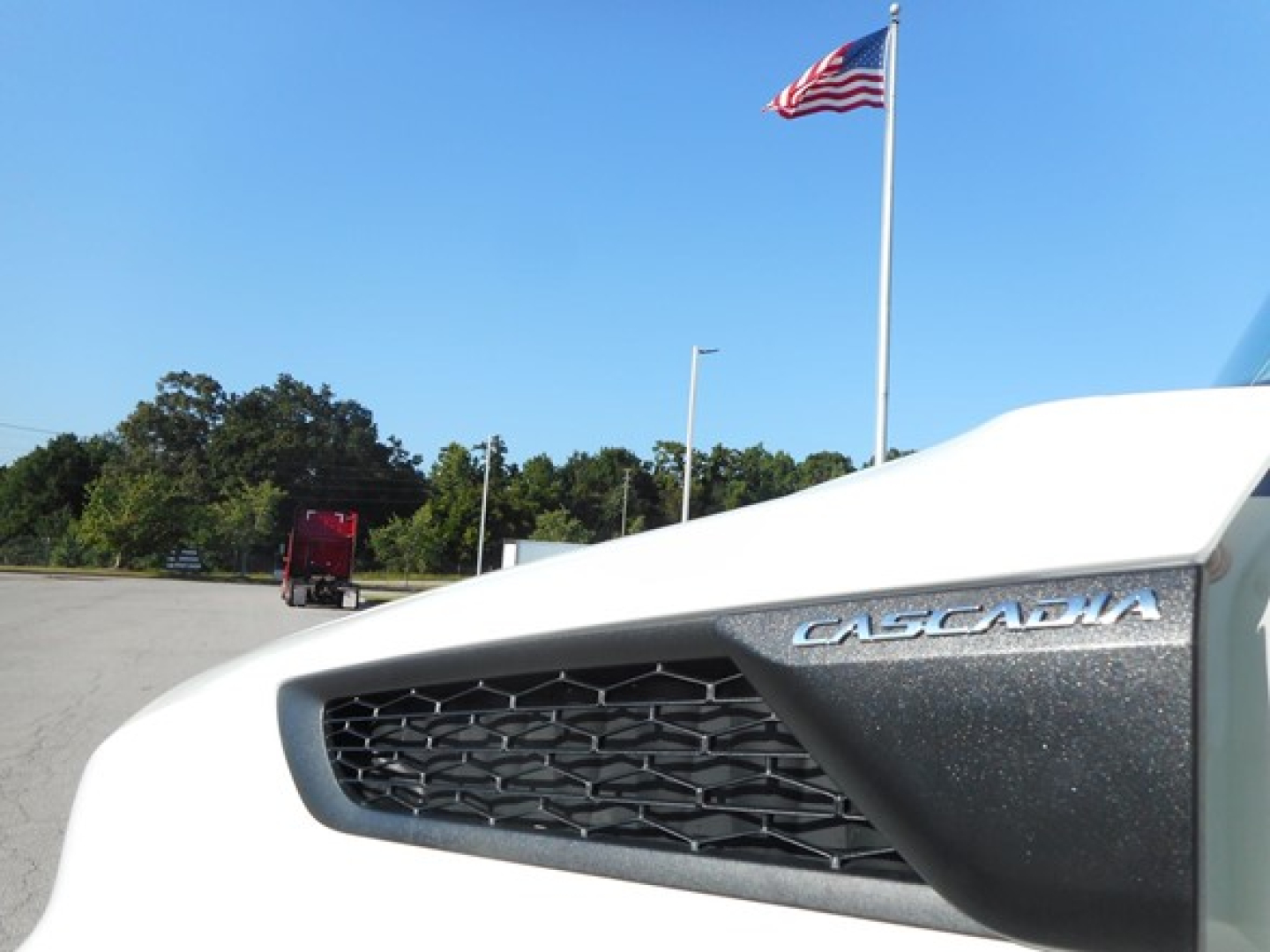 Front grille of a 2026 Freightliner Cascadia 126 truck with CASCADIA badge visible on the hood and an American flag in the background.