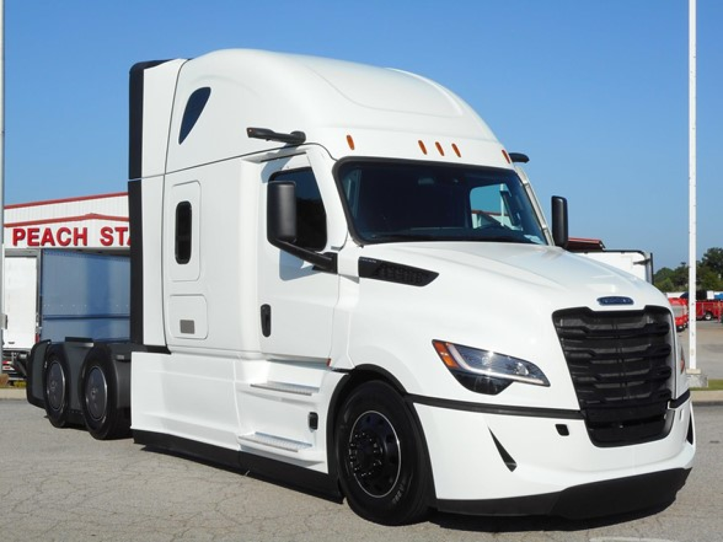 Truck in a dealership lot showing a white Freightliner Cascadia 126 semi-truck with aerodynamic cab and large black grille.