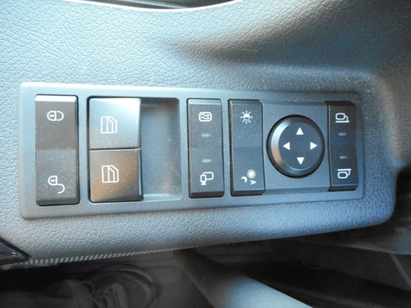 Panel of switches in Freightliner Cascadia showing multiple buttons for lights and mirrors with circular joystick control.