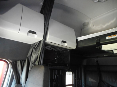 Inside Freightliner Cascadia cab showing overhead compartments and curtain area, with storage boxes and a ladder-like rack.