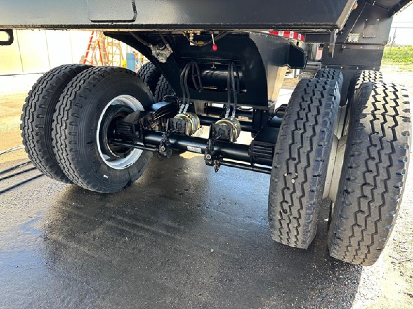 Dual-axle rear undercarriage of a dump trailer showing wheels, suspension, and drivetrain components.