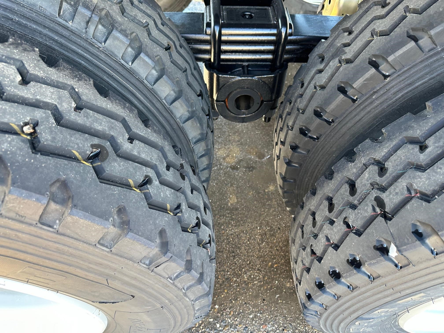 Twin rear axles with heavy-duty off-road tires and suspension visible in a frameless end dump trailer; center mounting components and hitch area visible between tires.