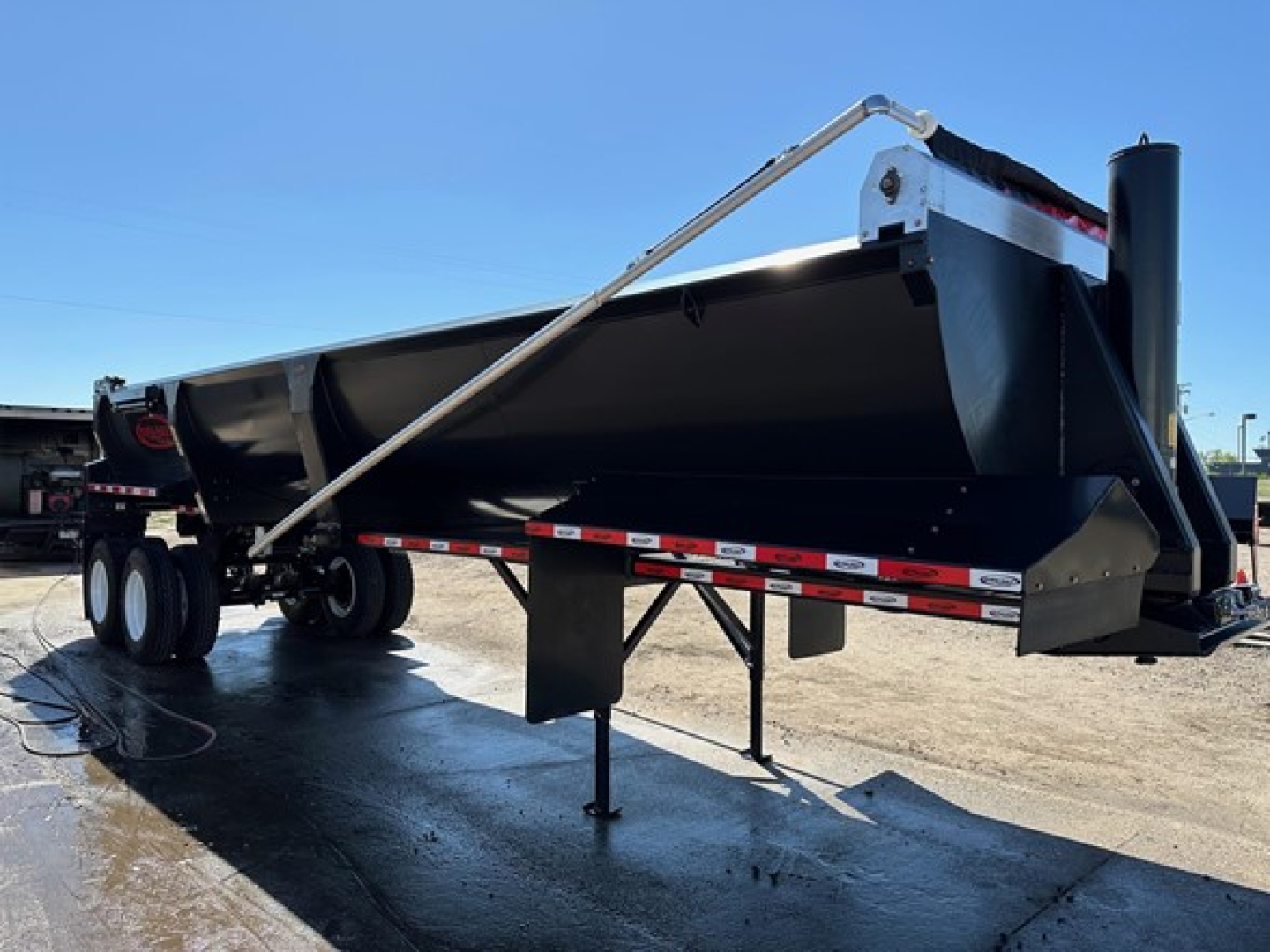 Dura Haul frameless end dump trailer showing a long black steel box, front hitch area, dual rear axles, and a support jack in the middle. Visible text on components not legible.