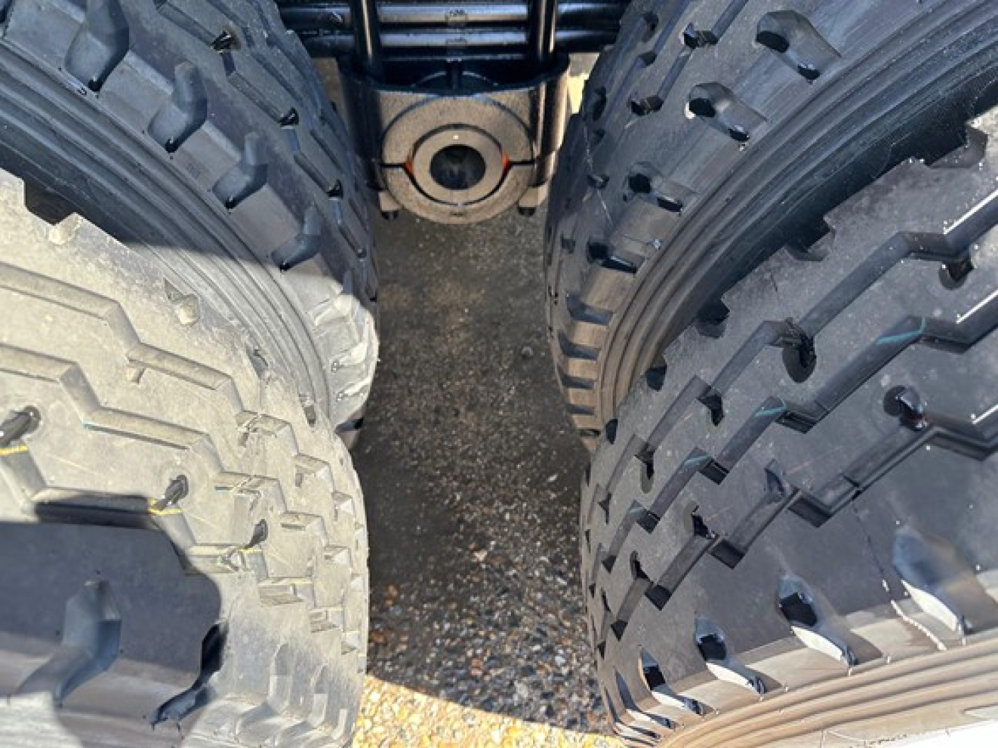 Frameless end dump trailer hitch area between dual tires showing suspension hanger and mounting eyelet.