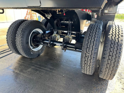 Dual-axle rear undercarriage of a dump trailer showing wheels, suspension, and drivetrain components.