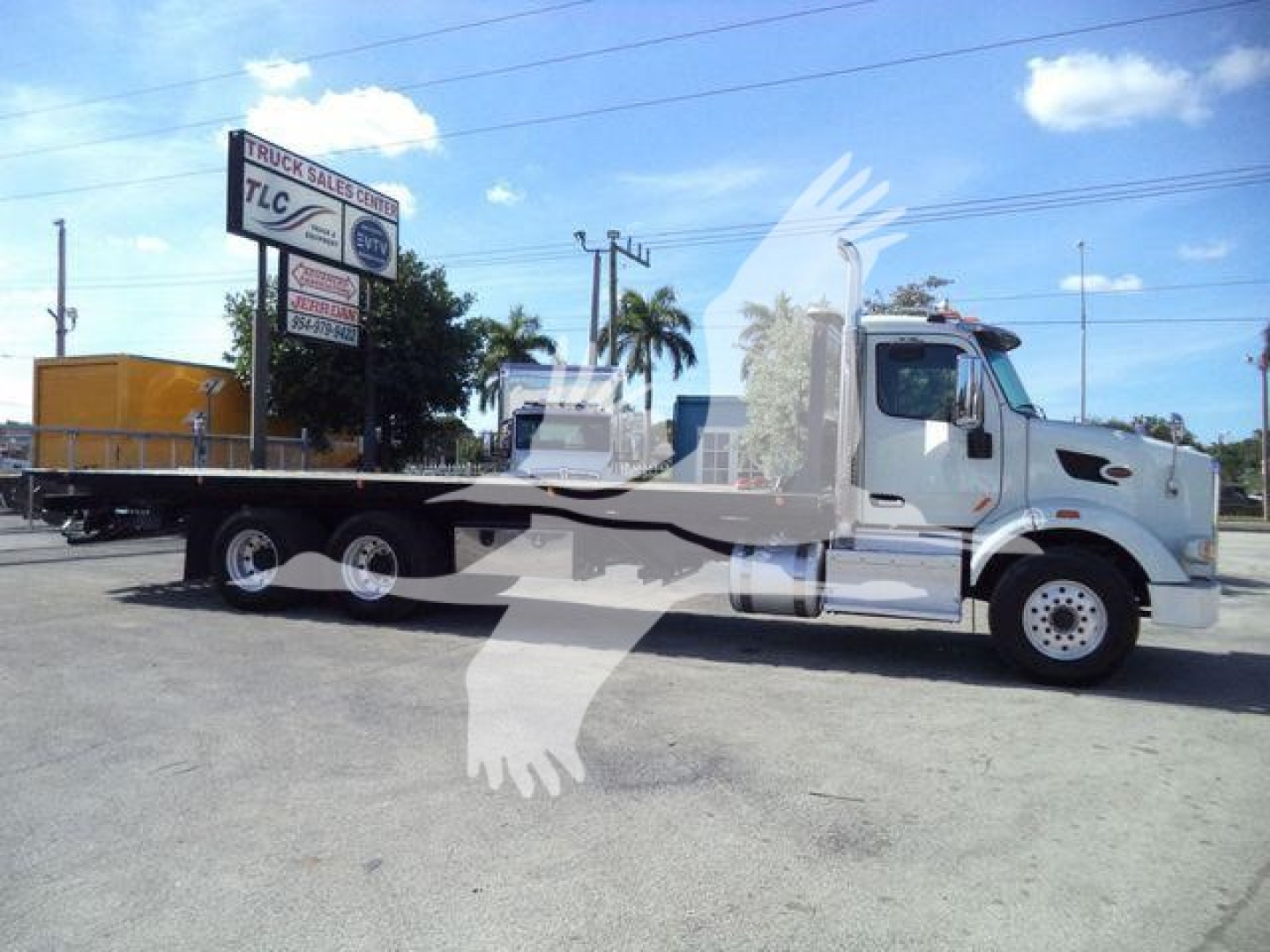 Peterbilt 567 rollback truck side view showing flatbed with chrome cab and wheels and a yellow load container in background