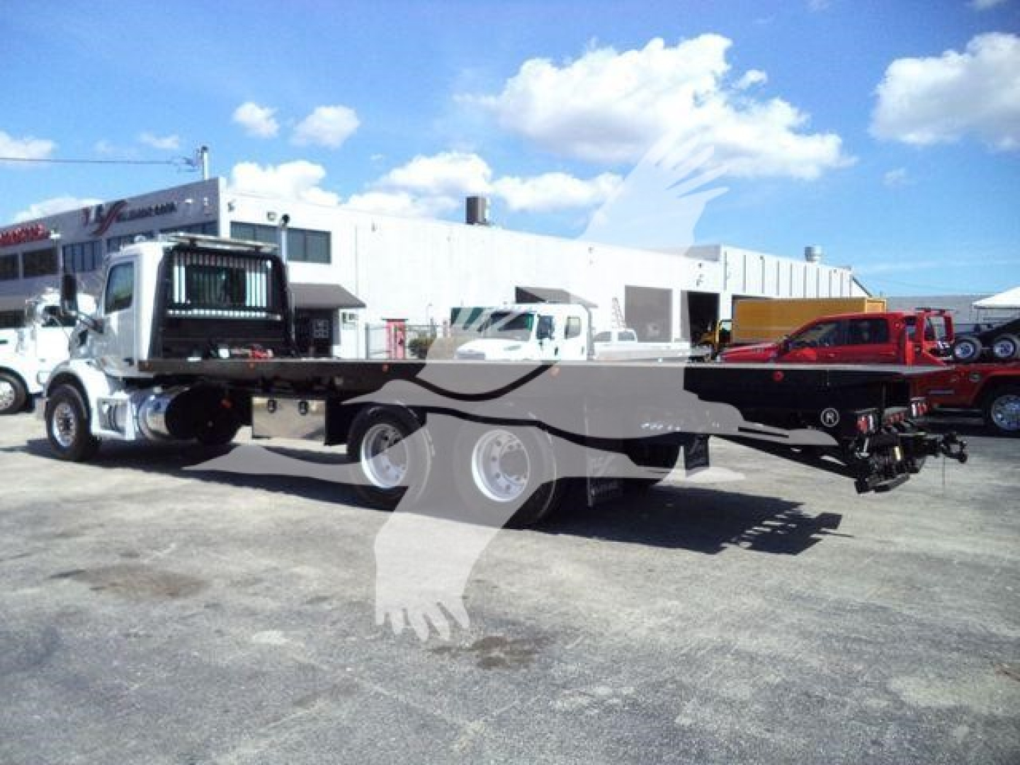 Peterbilt 567 rollback truck in a lot with equipment in background; no legible model text visible on stickers or controls.