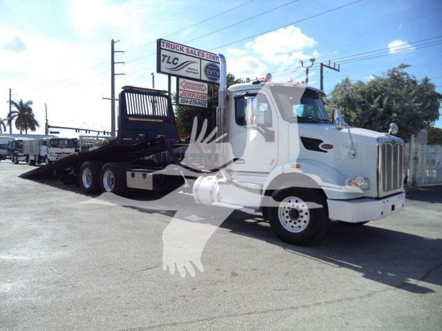 Peterbilt 567 rollback truck side-view showing flatbed with wheel-lift surface and cab with light bar, white exterior.