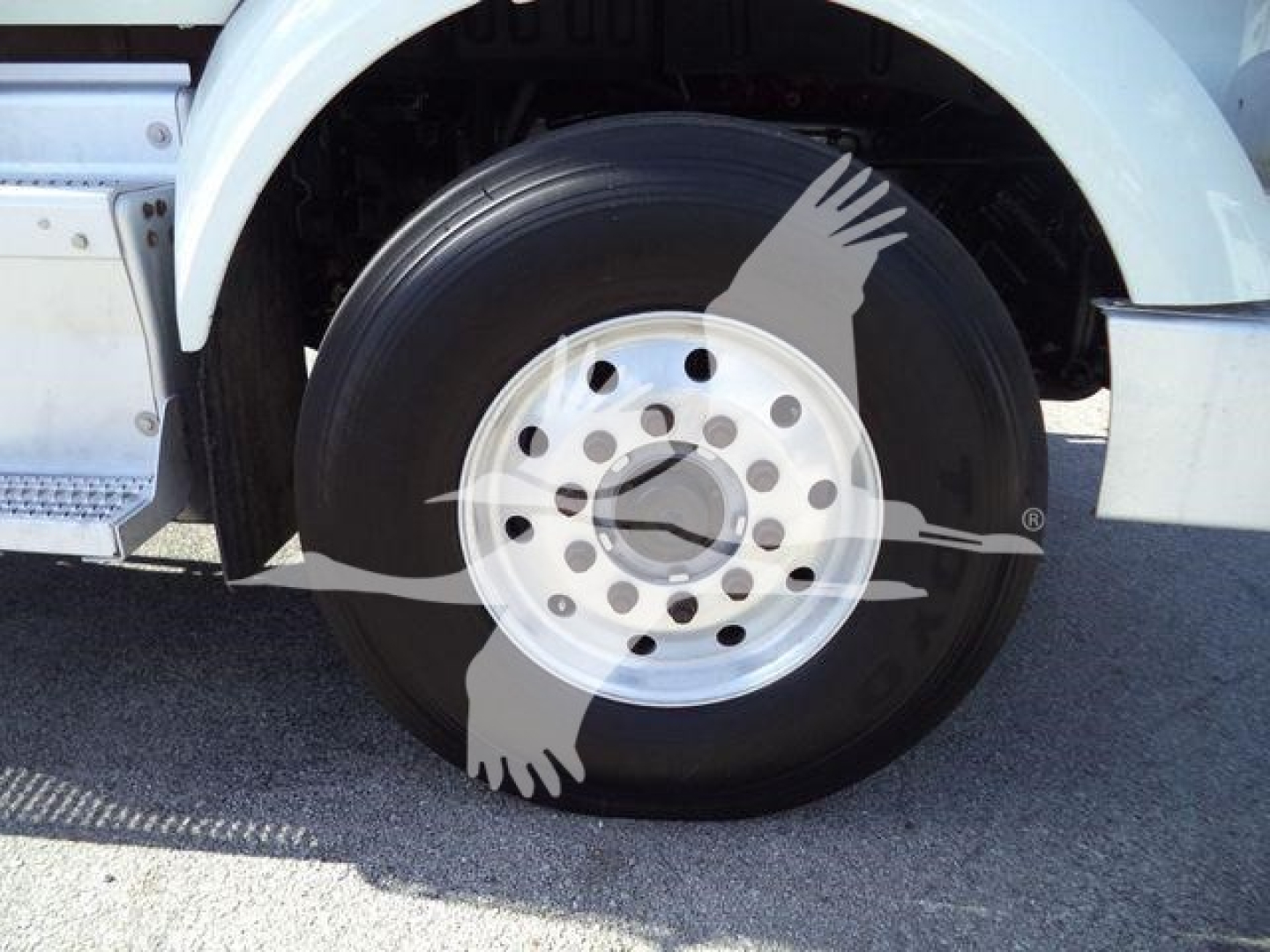 Peterbilt truck wheel and fender close-up showing front axle and wheel with a circular hubcap.