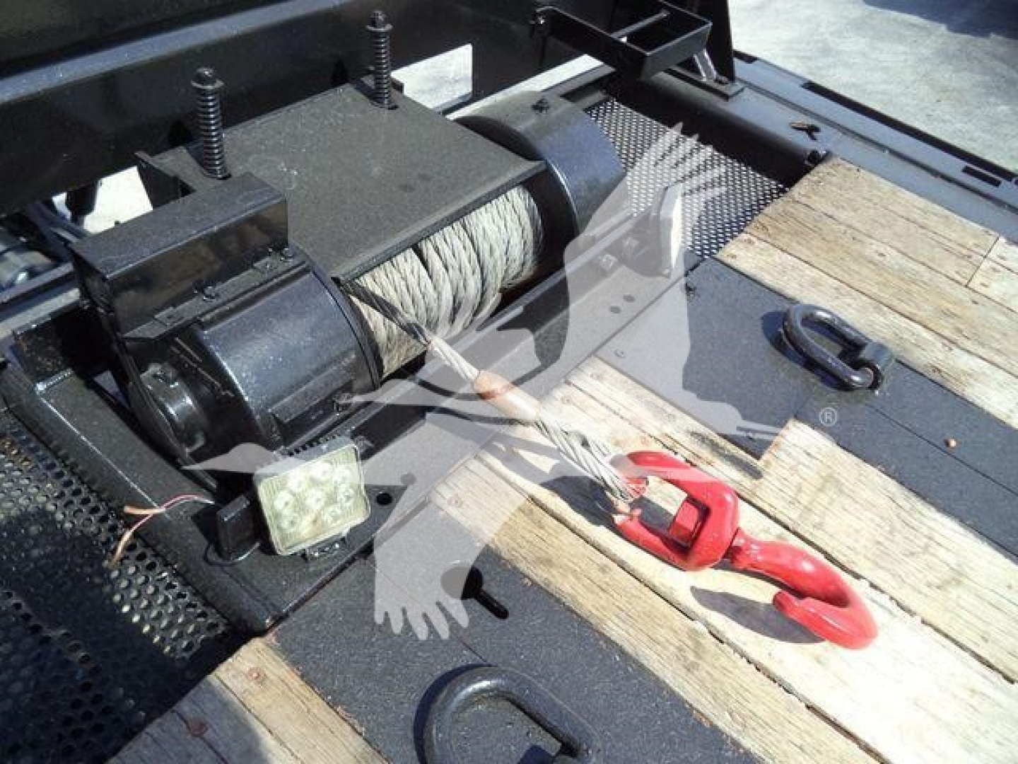 Winch system on a rollback truck bed with steel cable drum, motor, and red-handled hook visible.