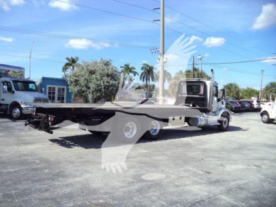 Truck tractor 2016 Peterbilt 567 rollback w/ flatbed trailer in lot, side view showing cab and long deck.