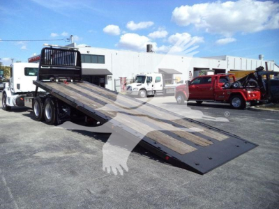 Peterbilt 567 rollback truck with a lowered flatbed in a parking lot, showing a long black tilt-bed and wheel-lift area.