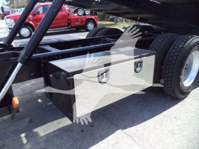 Peterbilt 567 rollback truck chassis showing a silver underbody toolbox mounted between the cab and rear dual wheels.