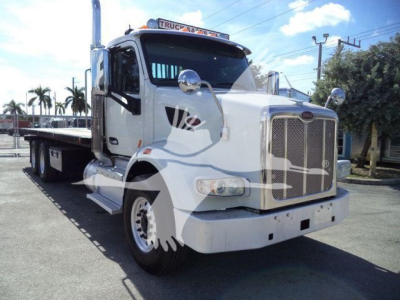 Peterbilt 567 truck in white, front three-quarter view with flatbed rollback, chrome grille, dual mirrors, and Peterbilt badge visible.