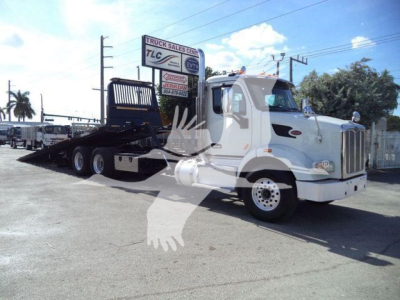 Peterbilt 567 rollback truck side-view showing flatbed with wheel-lift surface and cab with light bar, white exterior.