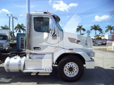 Peterbilt 567 sleeper cab truck side view with chrome exhaust stack and fuel tanks, silver/gray paint, white background with palm trees.