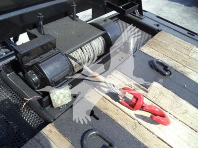Winch system on a rollback truck bed with steel cable drum, motor, and red-handled hook visible.