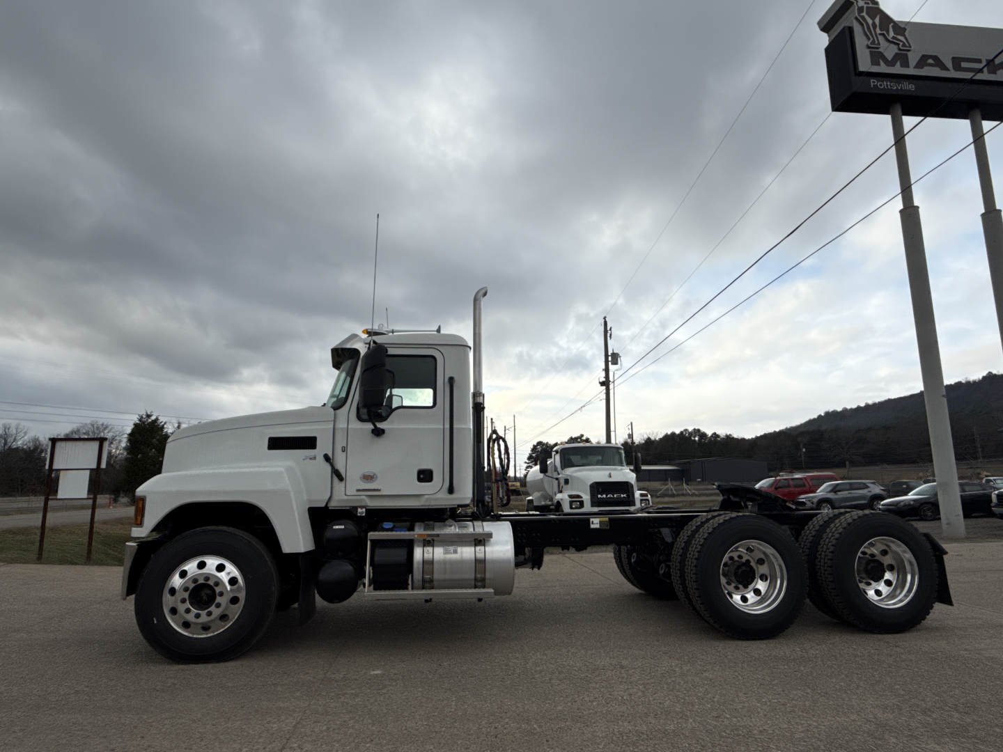 Truck side view of a 2026 Mack PI64T conventional daycab showing truck cab, dual rear axles, fuel tanks, and empty tractor frame.