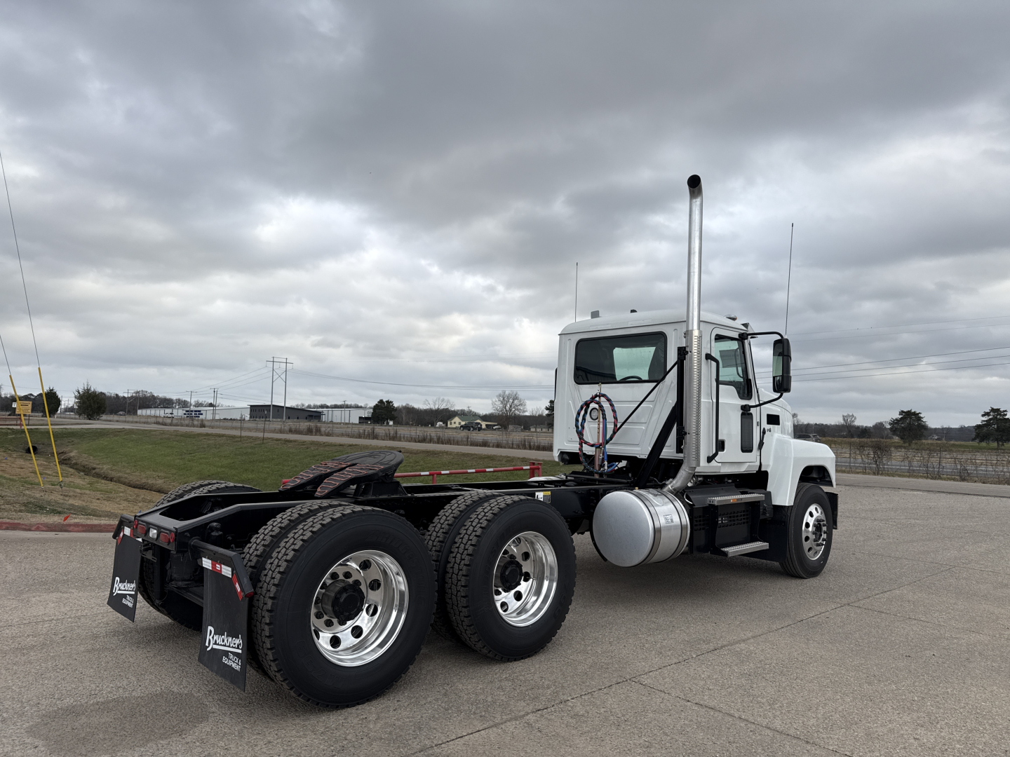 2026 Mack PI64T conventional daycab tractor side/rear view showing dual rear axles, exhaust stack, fuel tank, and chrome wheels.