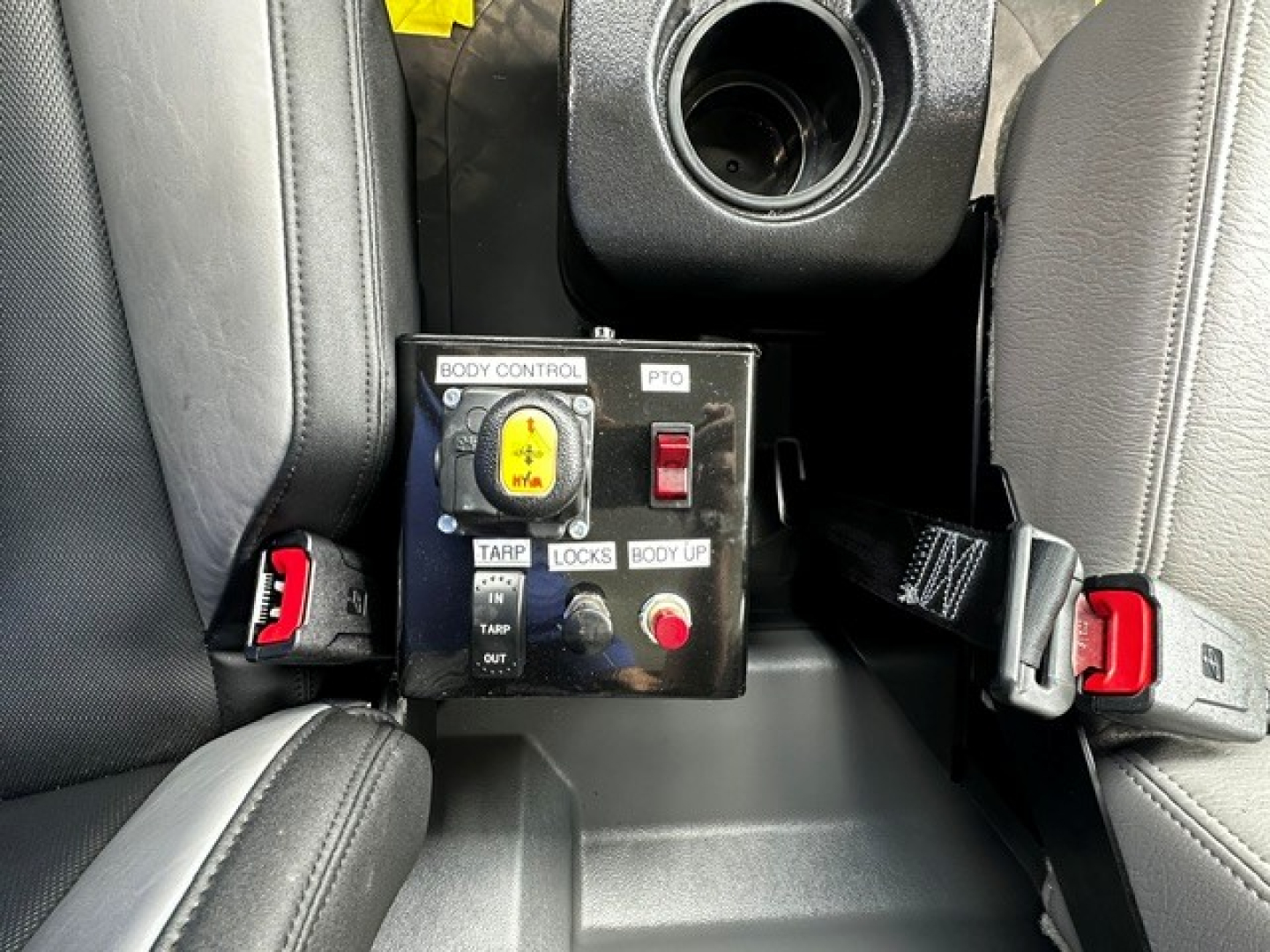 Mack MD7 truck interior center console showing body control panel with PTO switch, TARP, LOCKS, BODY UP, and red seat belt buckles.