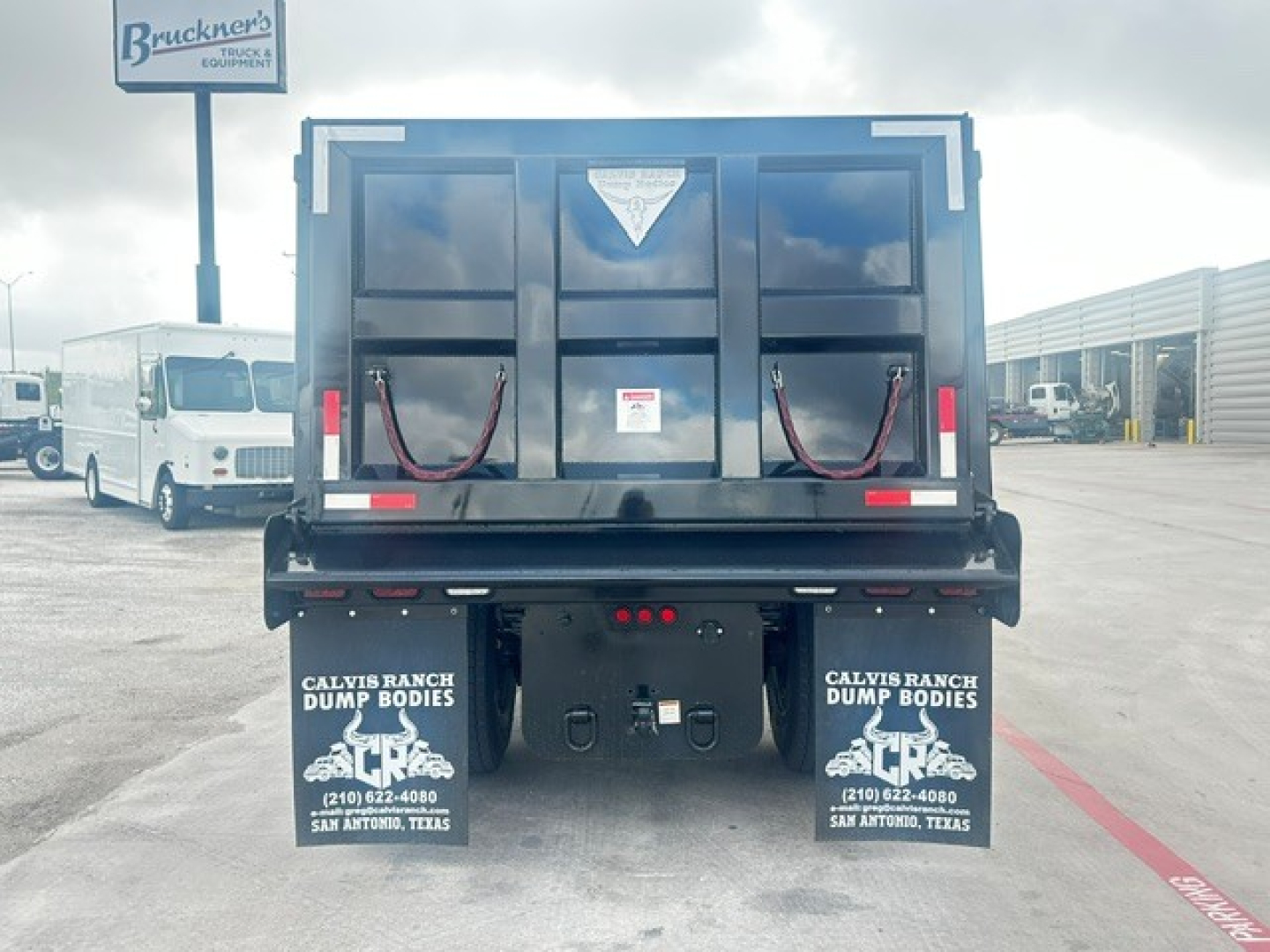 Rear view of 2027 Mack MD7 dump truck in new condition showing dump bed and bumper with decals, tail lights, and mud flaps.